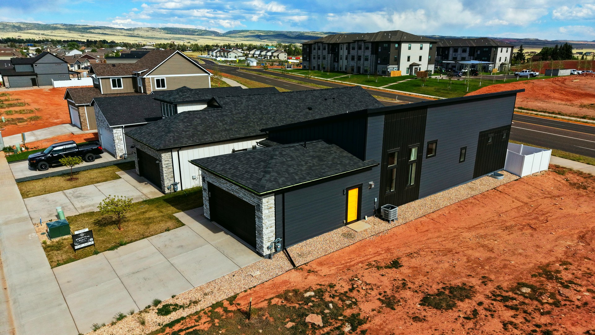 Aerial drone still of the front of a newly built modern home in Laramie, Wyoming with a for-sale sign, under a summer cloud bank